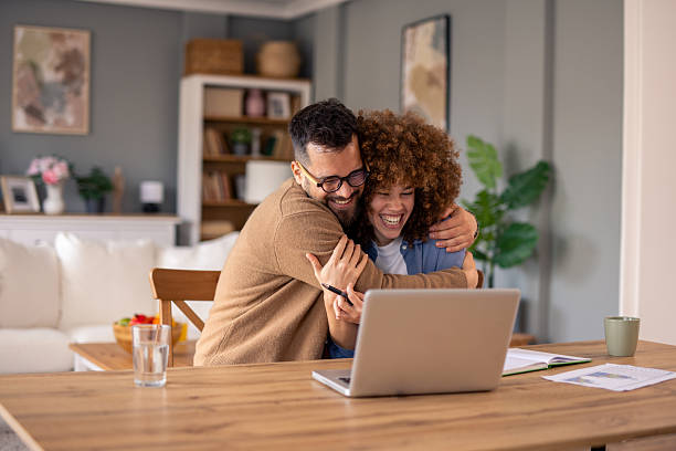 istock Joyful Couple Hugging While Celebrating Success in Cozy Home with Modern Laptop 2215548635