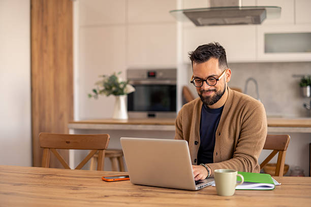 istock Focused Bearded Man with Glasses Working on Laptop at Bright Kitchen Table 2215548648