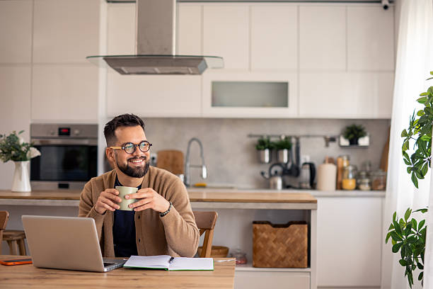 istock Mid-Aged Professional In Brown Sweater Enjoys Coffee Break While Working From Modern Kitchen 2215548658