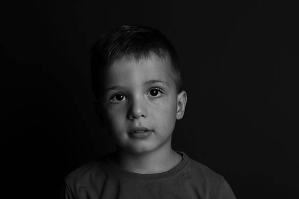 istock Portrait of sad little boy on dark background. Black and white effect 2215548700