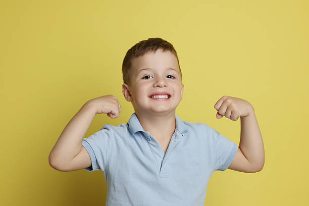istock Cute little boy showing his biceps on yellow background 2215548740