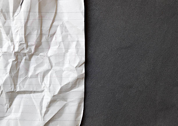 Old, torn ripped wrinkled crumpled folded discarded abandoned waste white paper lined blank empty page from notepad placed on horizontal black textured background making halved border backdrop with copy space for office presentation templates.