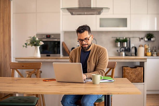 istock Mid-Aged Professional In Cardigan Working On Laptop In Contemporary White Kitchen 2215548868