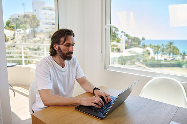 istock Bearded Young Man Working Remotely at Home with Scenic Ocean View Background 2215556070