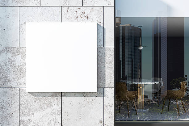 istock Blank square sign mounted on modern concrete wall outside a contemporary retail building with glass facade and city reflection in background. 3D Rendering 2215568974