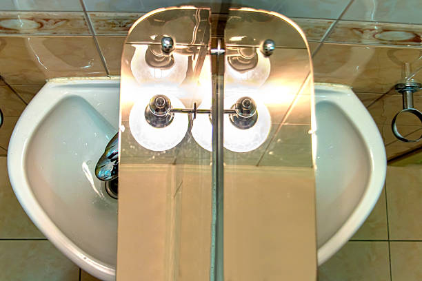 A mirror with shelf over sink and under lamp in a bathroom.