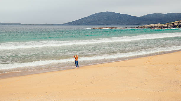 Woman walking along the shoreline at Nisabost beach on the west coast of Harris in the Outer Hebrides of Scotland.
