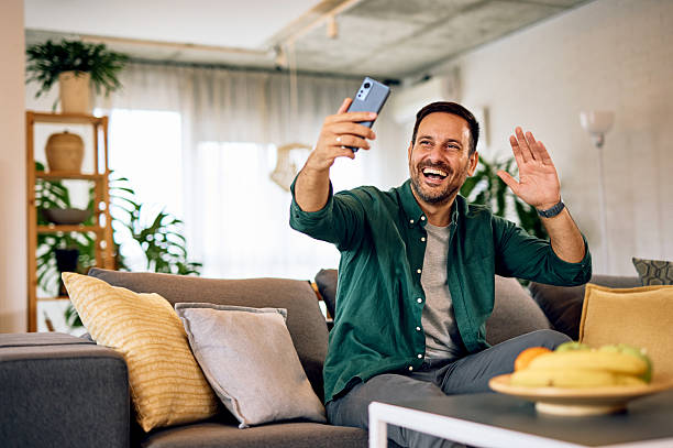 istock Happy man making a video call from home waving at the camera 2215571414