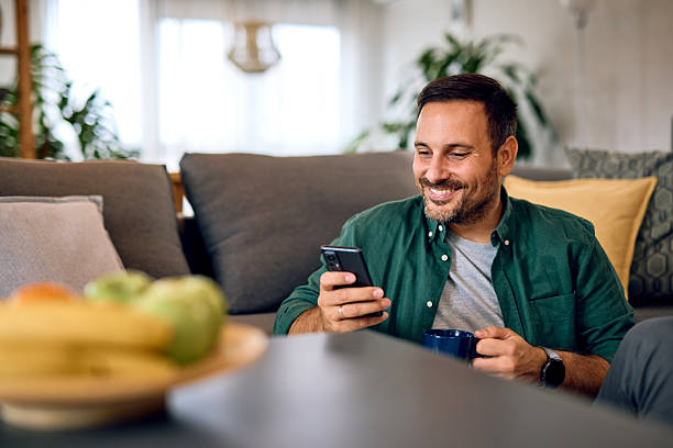 istock Smiling man using phone and drinking coffee at home 2215571436