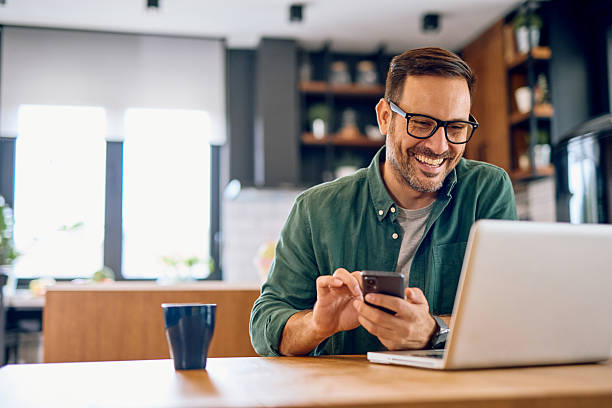 istock Smiling man using laptop and smartphone at home 2215571446