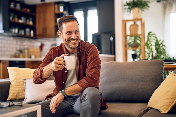 istock Smiling man relaxing on sofa drinking coffee at home 2215571502