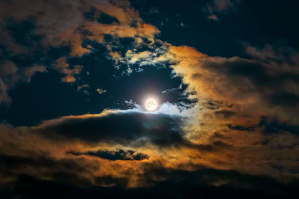 Full moon surrounded by colorful glowing clouds in beautiful night sky. In meteorology, a corona (plural coronae, Lunar aureole) is an optical phenomenon produced by the diffraction of moonlight in clouds