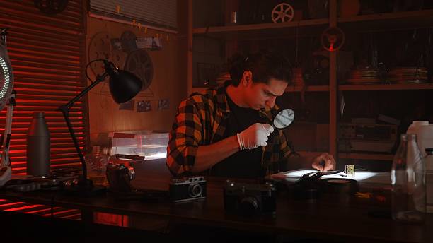 istock Young Man Analyzing Film Negatives in Dimly Lit Room 2215590664