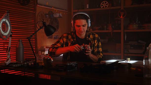 istock Young Man with Headphones Examining Camera in Retro Photography Studio 2215591321
