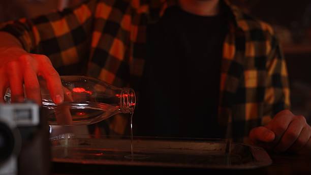 istock Person Pouring Liquid from Glass Bottle on Dimly Lit Table 2215592401