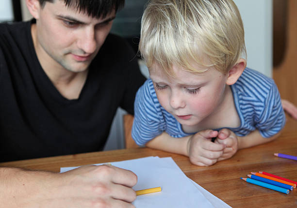 closeup portrait of father and toddler son drawing together at home bonding .