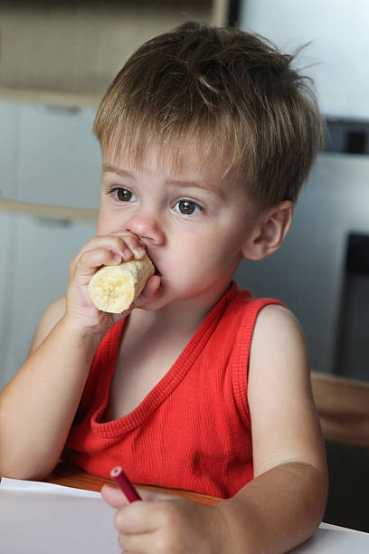 Close-up of a boy in vintage cap biting a loaf of bread while sitting on a hay bale. Rustic countryside snack moment.