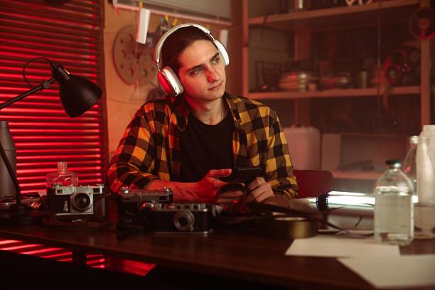 istock Young Man with Headphones Examining Camera in Retro Photography Studio 2215593627