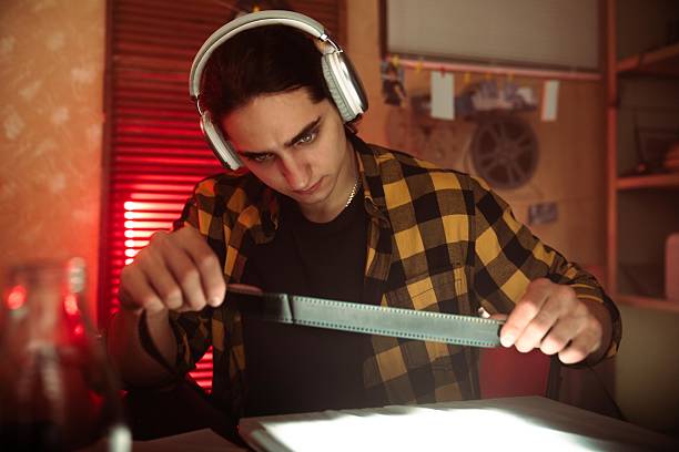 istock Young Man with Headphones Examining Camera in Retro Photography Studio 2215593861