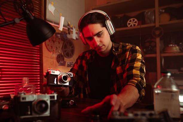 istock Young Man with Headphones Examining Camera in Retro Photography Studio 2215595049