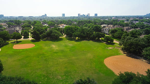 istock Baseball fields in inner suburb park with midtown Dallas skylines background, lush green upscale residential community luxury mansion houses established Preston Hollow mature landscaping, Texas 2215600410