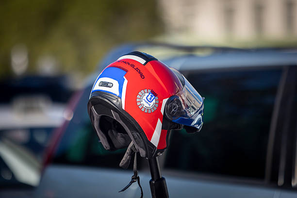 April 28, 2025. Madrid, Spain. A brightly colored helmet belonging to a Madrid municipal mobility agent rests on a scooter or parked vehicle. Featuring the official insignia and a red, blue, and white design, the helmet stands out against the blurred urban background. A symbol of the city's traffic management and street-level public service presence.