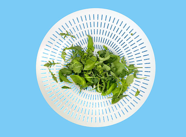 Fresh arugula and spinach in a white colander, top view, isolated on a bright blue background. Healthy eating, vegetarian food concept. Minimal flat lay.