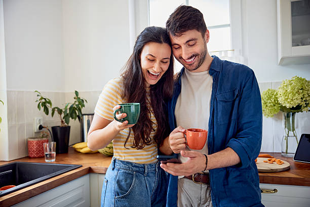 istock Excited couple looking at mobile phone in kitchen while having coffee 2215652850