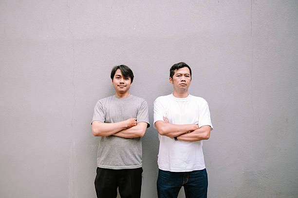 istock Two men standing with arms crossed against gray wall backdrop looking ahead 2215657504