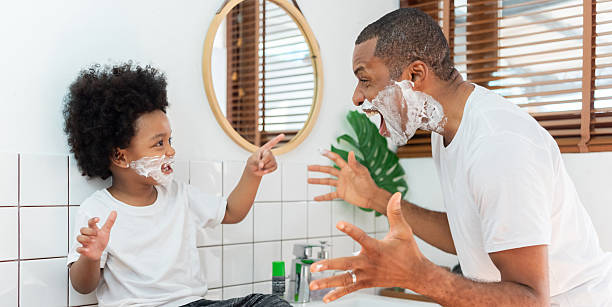 istock African American father playfully interacts with his son while both are engaged in a morning shaving routine. sharing laughter in a white bathroom. 2215657769