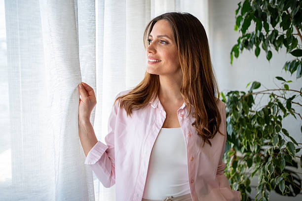 istock Smiling woman opening curtains and looking out the window 2215660974