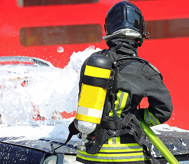 istock Firefighter with   oxygen cylinder on his shoulders that sprays   foaming white on   car to extinguish   fire after   road accident 2215670134