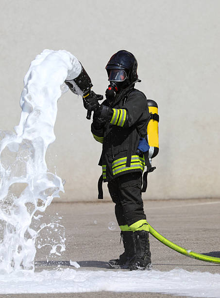 istock Firefighter with Protective Mask and Oxygen Bottle as he operates  lance which sprays white extinguishing foaming agent 2215670346
