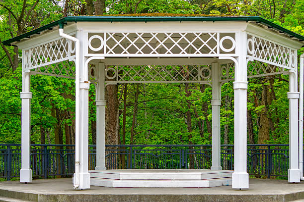 White decorative park gazebo with a green forest background. Classic garden architecture, a place for rest and gatherings surrounded by nature.