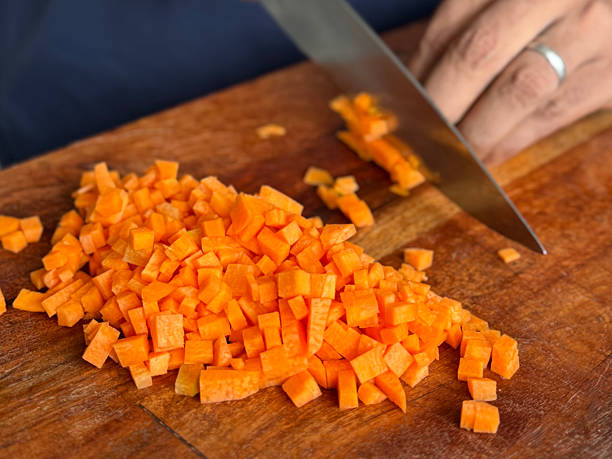 Stock photo showcases a professional chef expertly dicing fresh carrots, leeks, and onions on a rustic wooden breadboard. The chopped vegetables are prepared for a comforting stew, casserole, or homemade dinner