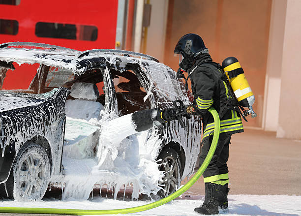 istock Firefighter with   protective helmet and oxygen tank while spraying   foam to extinguish   fire of   crashed vehicle after   road accident 2215672337
