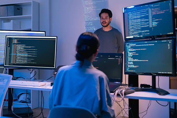 istock young Asian software development manager leads a late-night office discussion with his executive team, mentoring developers and analyzing source code to guide programming and project development 2215674522