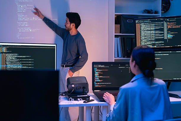 istock young Asian software development manager leads a late-night office discussion with his executive team, mentoring developers and analyzing source code to guide programming and project development 2215674523