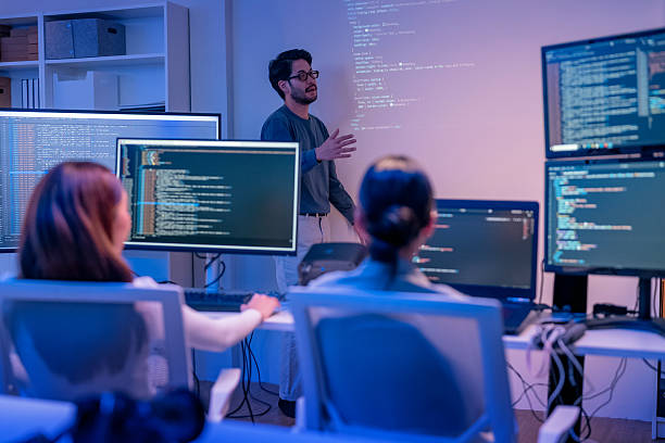 istock young Asian software development manager leads a late-night office discussion with his executive team, mentoring developers and analyzing source code to guide programming and project development 2215674528