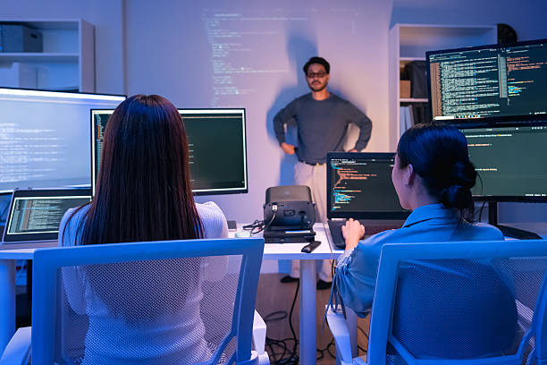 istock young Asian software development manager leads a late-night office discussion with his executive team, mentoring developers and analyzing source code to guide programming and project development 2215674576