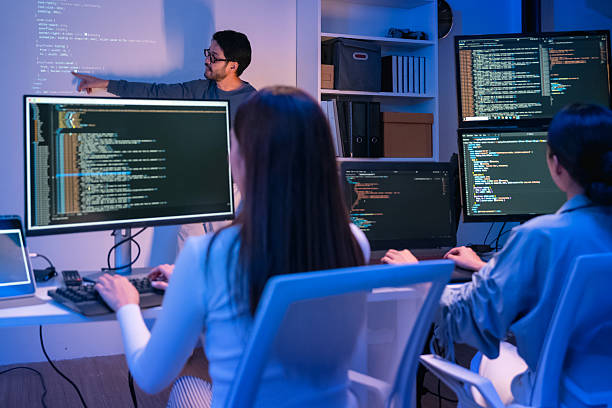 istock young Asian software development manager leads a late-night office discussion with his executive team, mentoring developers and analyzing source code to guide programming and project development 2215674580