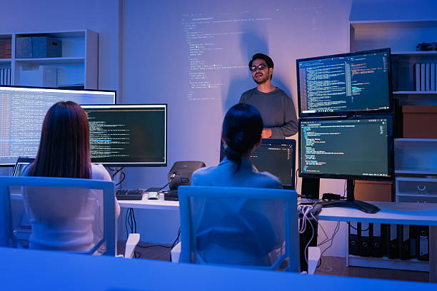 istock young Asian software development manager leads a late-night office discussion with his executive team, mentoring developers and analyzing source code to guide programming and project development 2215674590