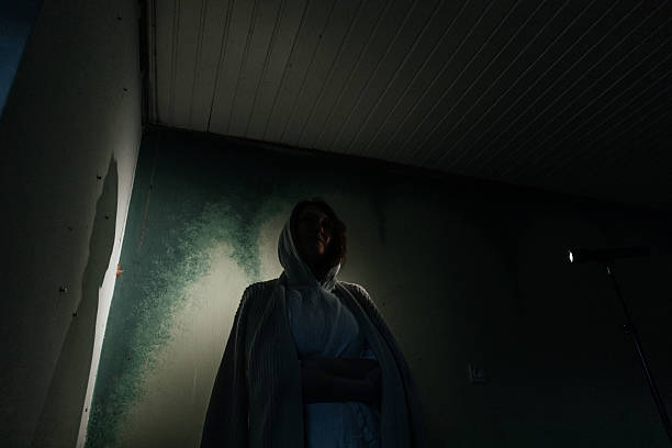 istock Mysterious female in hooded robe standing in dim light facing corner 2215674876