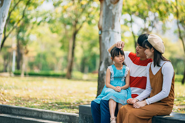An Asian family of three heads to the park for a picnic, indulging in games and blowing bubbles together. Their laughter echoes through the air as they enjoy quality time together, creating unforgettable moments filled with happiness and love.