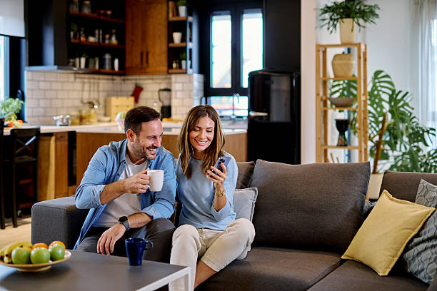 istock Couple relaxing on sofa, drinking coffee and using smartphone at home 2215677561