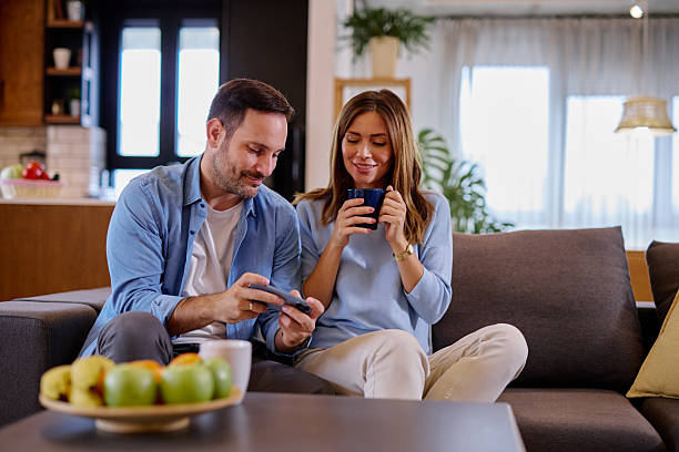 istock Young couple relaxing on the sofa, using phone and drinking coffee 2215677567