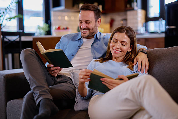 istock Happy couple reading books while relaxing on sofa at home 2215677681
