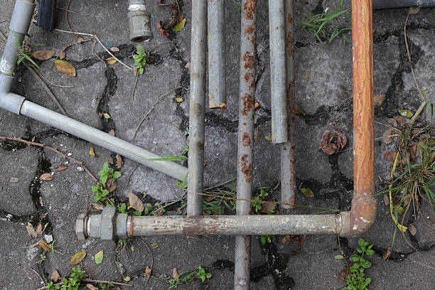 Close-up of rusty metal pipes lying on cracked pavement with grass and scattered leaves, highlighting urban decay and neglect.
