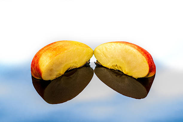 Two halves of a fresh apple rest mirrored on a reflective surface, showcasing crisp textures, sweet allure, and a subtle nod to orchard tradition in minimalist style