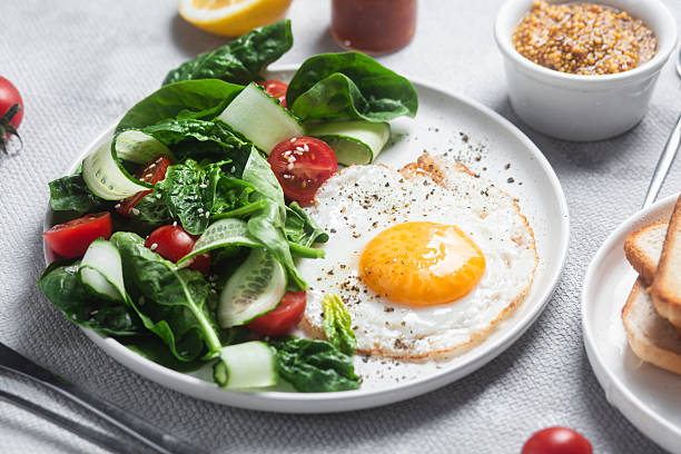 istock Fried egg with spinach, tomato and cucumber salad in a white plate. Healthy breakfast 2215696658